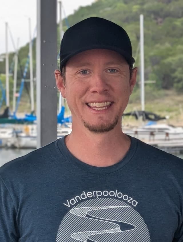Allan grinning in a black cap at a sailboat marina